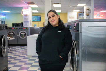 Woman leans against washing machine at Blue Lagoon Laundry