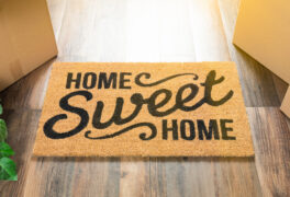 Doormat on sun-drenched wood floor that says 