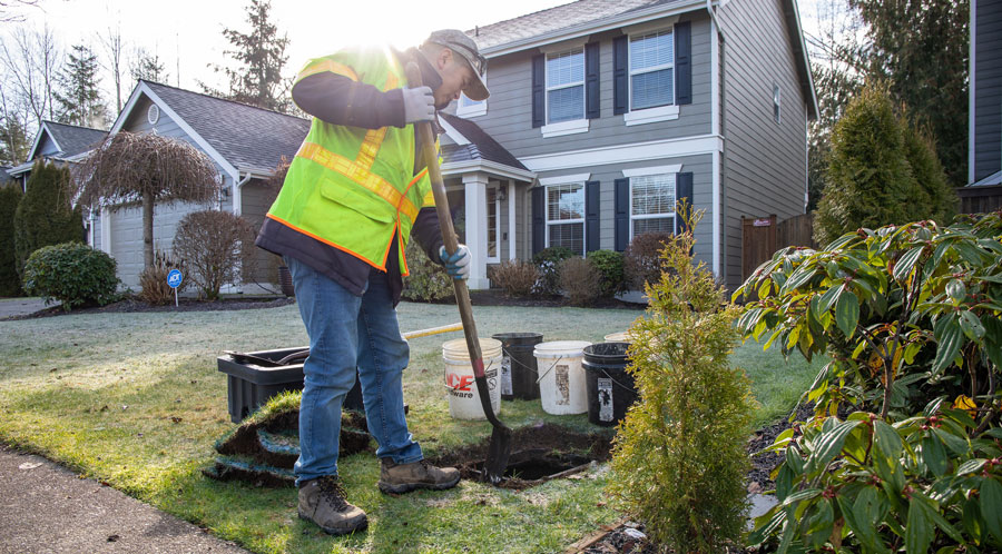 A man digs a hole in a yard to drop in a water meter box