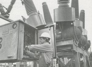 Man works in a cabinet with large electrical equipment behind him