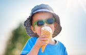 Little boy in bright green sunglasses enjoys ice cream on a hot summer day