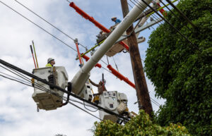 Line workers in buckets perform grid maintenance against a bright blue sky