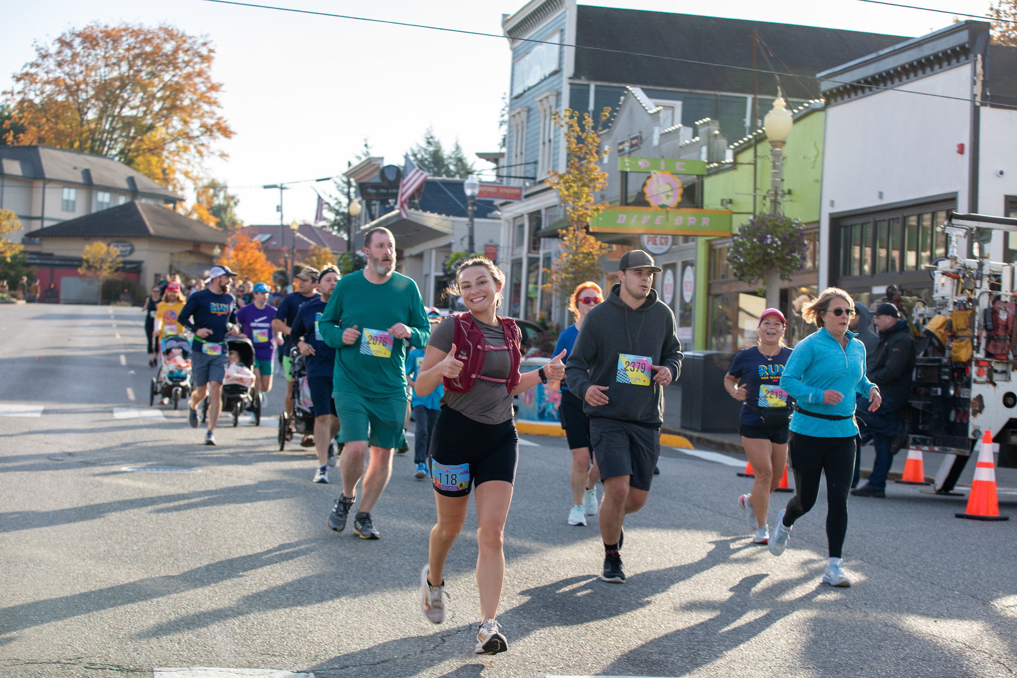 A racer gives a thumbs up as she runs down First Street in the company of other runners.