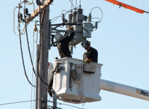 Two lineworkers in a bucket install a recloser on a utility pole